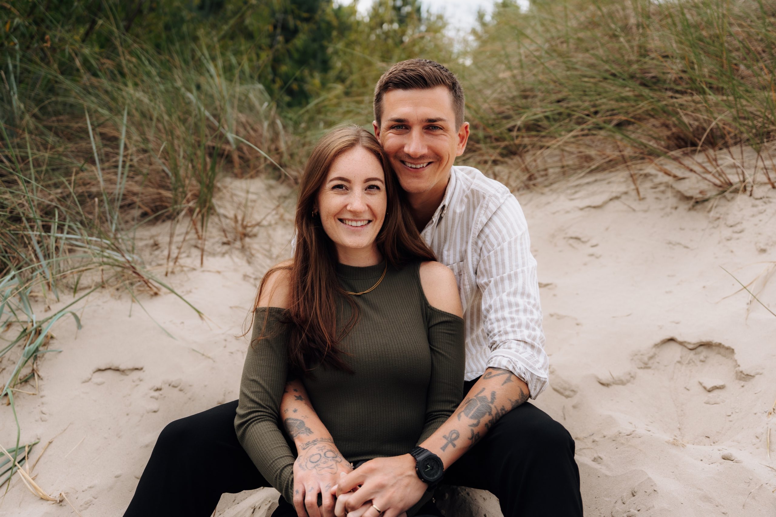 Stephie und Robert von Pure Weddings sitzen lächelnd in den Sanddünen