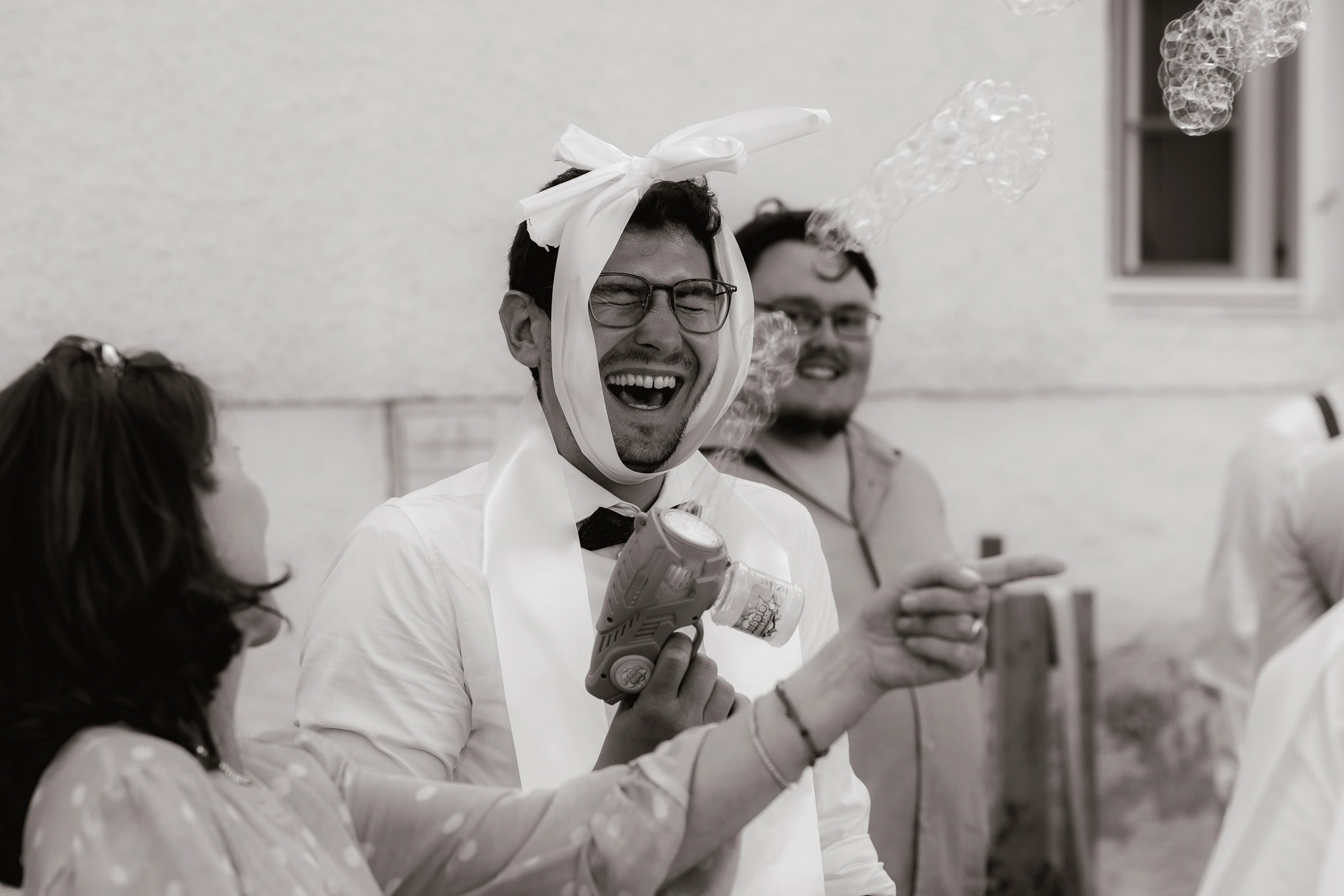 herzhaft lachender Hochzeitsgast mit Band um dem Kopf und Seifenblasenmaschine