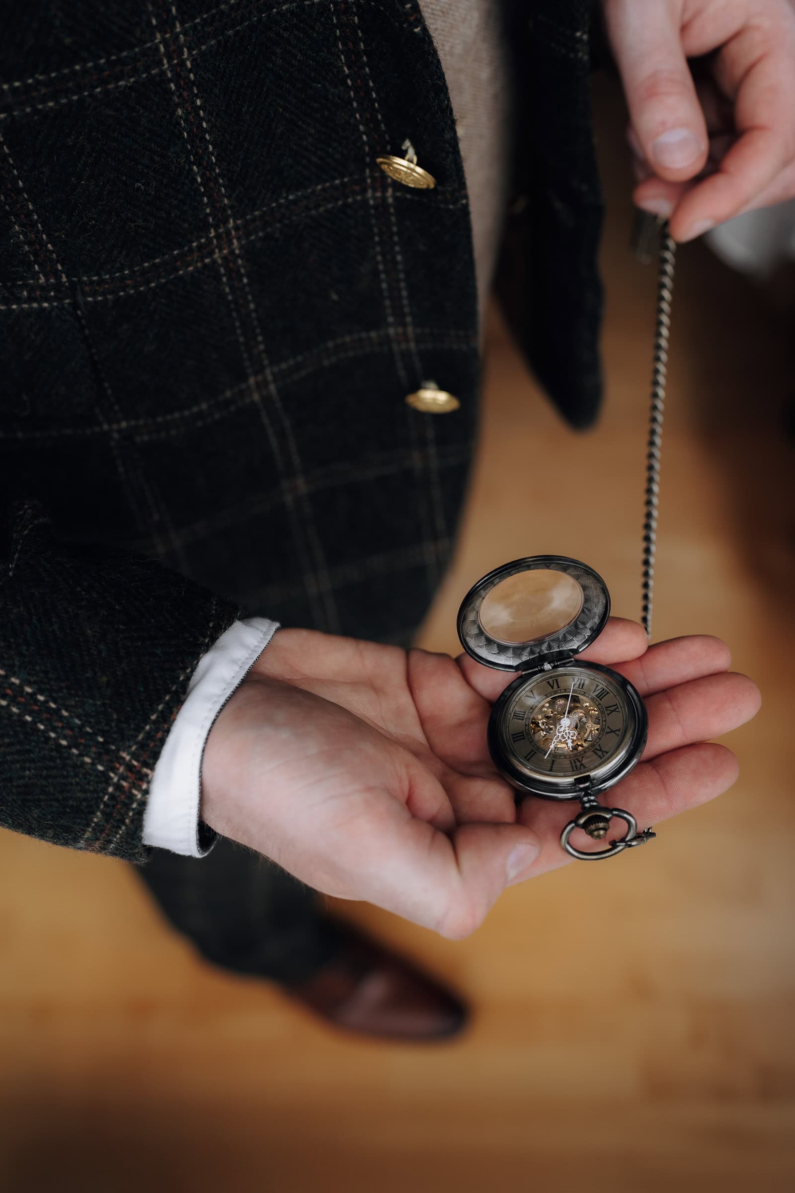 Detailaufnahme einer eleganten Taschenuhr in der Hand des Bräutigams im Tweed-Sakko bei einer Vintage Hochzeit in Freising