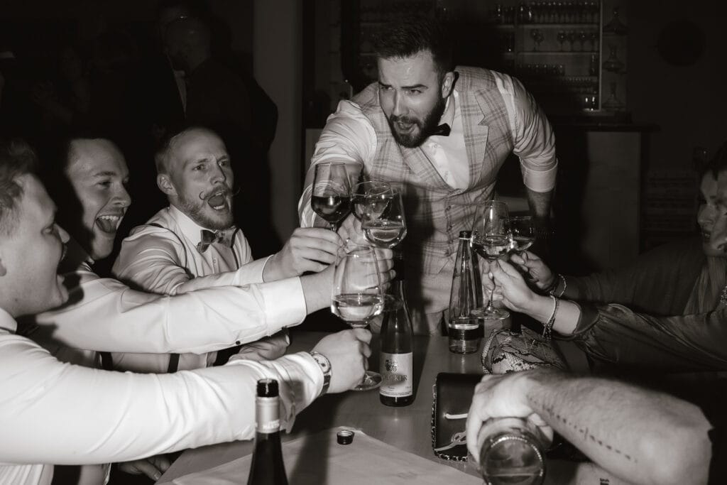 Gruppe von Männern stößt lachend mit Bräutigam an. Hochzeitsfeier Freising Maiers Hofstubn.