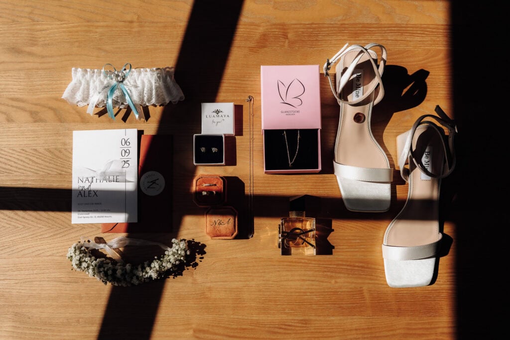 Stimmungsvolles Flatlay der Hochzeitsdetails wie Brautschuhe, Schmuck und Einladung bei dramatischem Lichteinfall