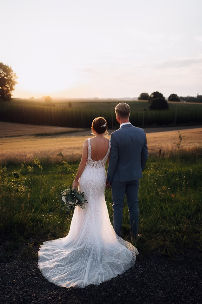 Hochzeitsfotograf Freising fängt ein Brautpaar von hinten im goldenen Abendlicht auf einem Feld an der Eventtenne Pfaffenhofen ein