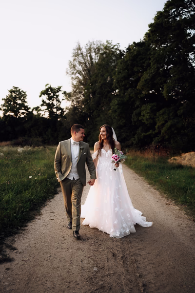 Brautpaar spaziert lachend auf einem Feldweg bei Gut Sedlbrunn, aufgenommen von einem Hochzeitsfotografen.