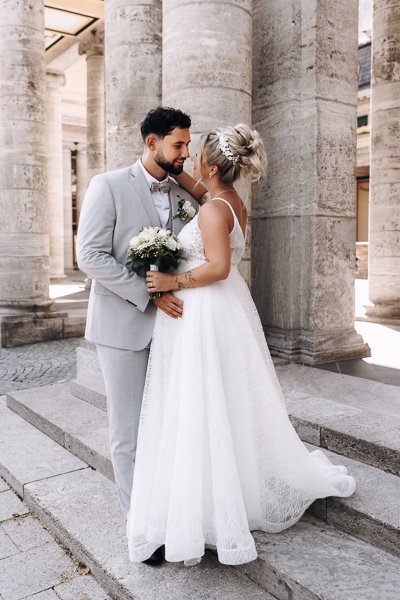 Hochzeitsfotograf Freising fotografiert ein schwangeres Brautpaar vor den historischen Säulen an der Mandlstraße in München.